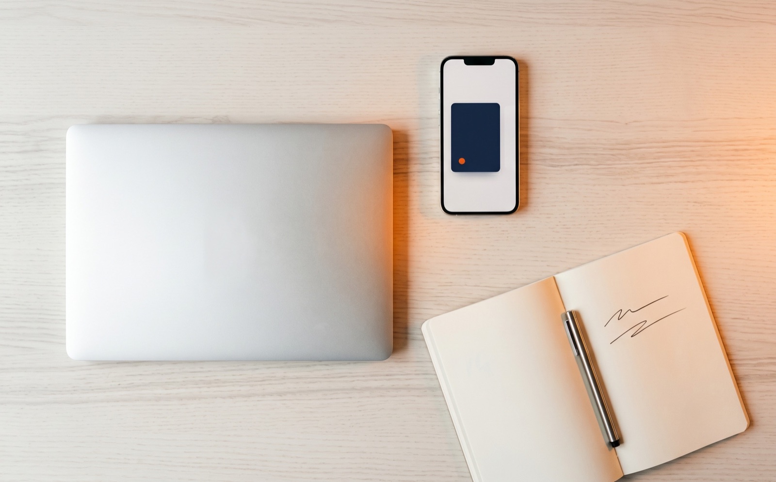 Stilleven van laptop, smartphone en notebook met pen op een warme houten desk, één oranje accent